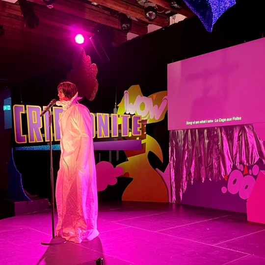 Roylesque is wearing a large white gown with oversized sleeves, a large collar and medium-length black hair. Yes, it's a wig.